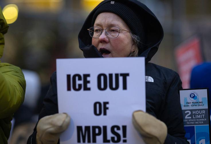 A photograph of a woman in winter gear holds an "ICE OUT of MPLS!" sign in her mittened hands.